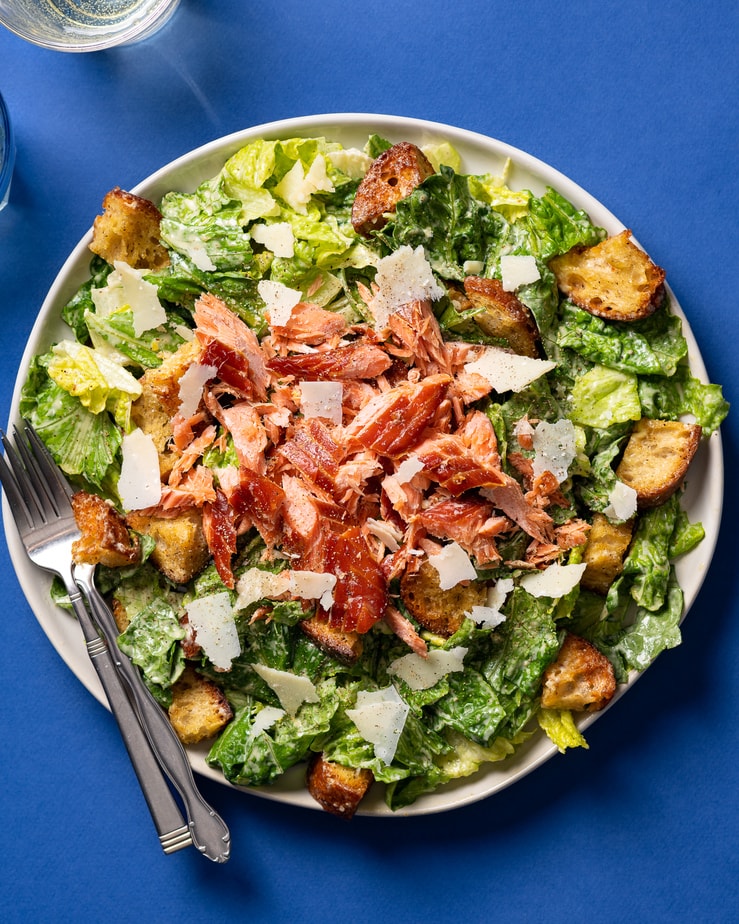 smoked salmon caesar salad on a white plate on a blue tablecloth